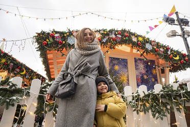 Lächelnde Mutter und Sohn auf dem Weihnachtsmarkt am Zaun - SSGF00952