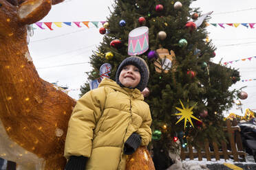 Junge mit Strickmütze neben einem geschmückten Hirsch auf dem Weihnachtsmarkt - SSGF00964