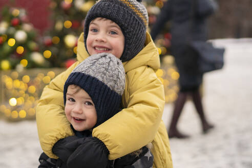 Lächelnde Brüder umarmen sich auf dem Weihnachtsmarkt - SSGF00970