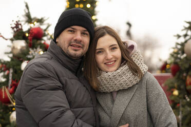 Lächelndes Paar in warmer Kleidung auf dem Weihnachtsmarkt - SSGF00971