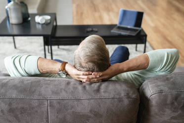 Man with hands behind head sitting on sofa at home - VPIF06074