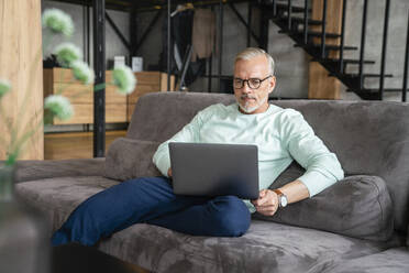 Businessman using laptop on sofa at home - VPIF06075