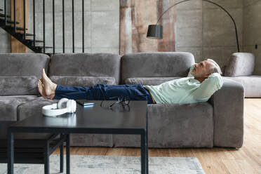 Man with hands behind head lying on sofa in living room at home - VPIF06082