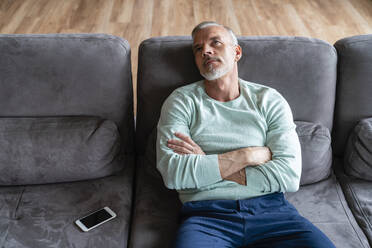 Exhausted man with arms crossed sitting on sofa at home - VPIF06089