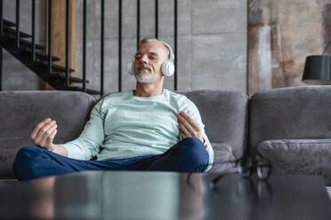 Mann hört Musik über kabellose Kopfhörer und meditiert auf dem Sofa - VPIF06096