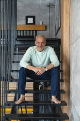 Smiling man sitting on staircase at home - VPIF06124