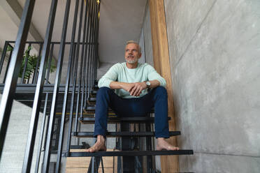 Thoughtful man sitting on staircase at home - VPIF06126