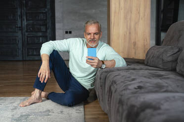 Älterer Mann, der ein Smartphone benutzt und sich zu Hause auf das Sofa lehnt - VPIF06136