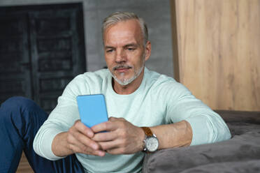 Mann mit Mobiltelefon am Sofa sitzend - VPIF06138