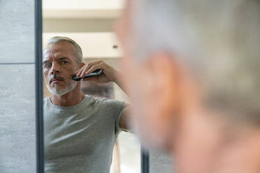 Man shaving beard with electric razor looking at mirror - VPIF06162