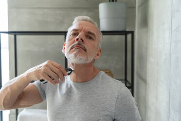 Man shaving beard with electric razor in bathroom - VPIF06164