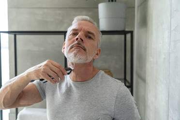 Mann rasiert Bart mit elektrischem Rasierapparat im Badezimmer - VPIF06164