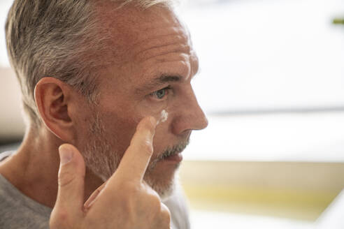 Man applying cream on face in bathroom - VPIF06165