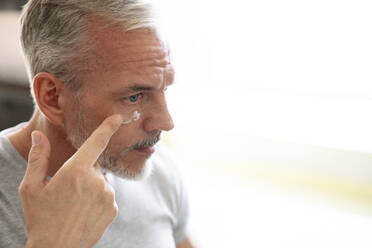 Man applying cream on face in bathroom at home - VPIF06166