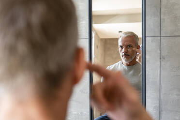 Man applying cream on face looking at mirror - VPIF06167