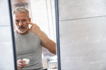 Man applying on moisturizer face looking at mirror in bathroom - VPIF06168