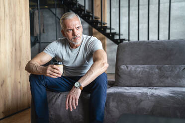 Man holding disposable cup sitting on sofa in living room - VPIF06174