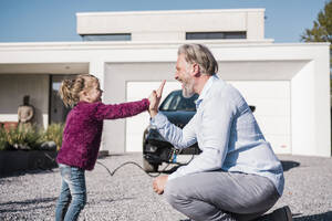 Happy girl giving high five to father in front of car on sunny day - MOEF04070