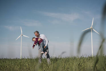 Verspielter Vater mit Tochter, die ein Windmühlenmodell auf einem Bauernhof hält - MOEF04114