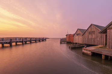 Deutschland, Mecklenburg-Vorpommern, Zingst, Pier und Reihe von Bootshäusern an der Küste in der Abenddämmerung - KEBF02280