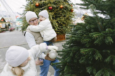 Vater und Töchter hängen Weihnachtsschmuck an den Baum - SIF00125