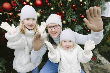 Lächelnder Vater mit Töchtern, die vor einem Weihnachtsbaum gestikulieren - SIF00133