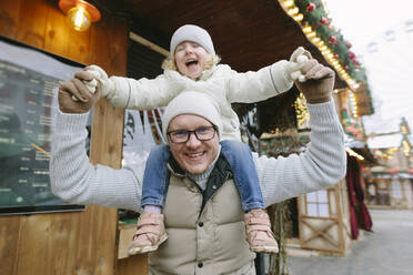 Lächelnder Vater trägt Tochter auf den Schultern auf dem Weihnachtsmarkt - SIF00136