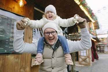 Glücklicher Vater trägt Tochter auf den Schultern auf dem Weihnachtsmarkt - SIF00137