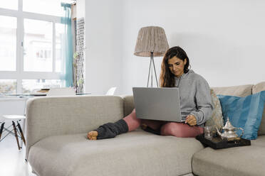 Mature freelancer using laptop sitting on sofa in living room at home - DCRF01191