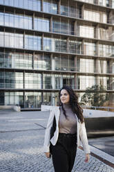 Young businesswoman walking in front of modern office building - DCRF01194
