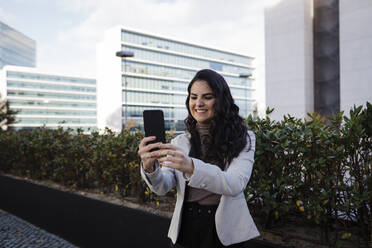 Lächelnde junge Geschäftsfrau, die ein Selfie im Finanzviertel macht - DCRF01197