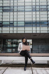 Engagierte junge Geschäftsfrau sitzt auf einer Bank und benutzt einen Laptop - DCRF01201