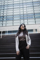 Smiling businesswoman standing on staircase in front of modern building - DCRF01207