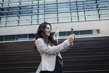 Happy businesswoman on video call through smart phone in front of office building - DCRF01209