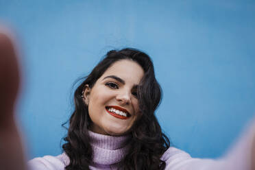 Schöne glückliche Frau, die ein Selfie vor einer blauen Wand macht - DCRF01210