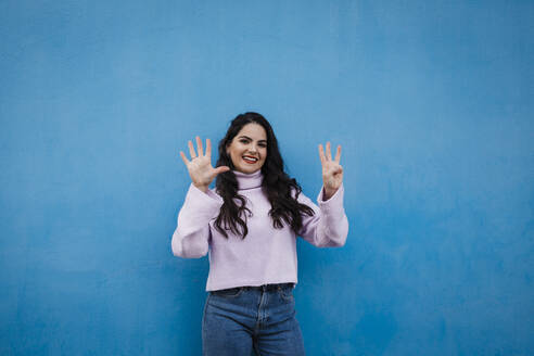 Smiling young beautiful woman showing number 8 in front of blue wall - DCRF01228