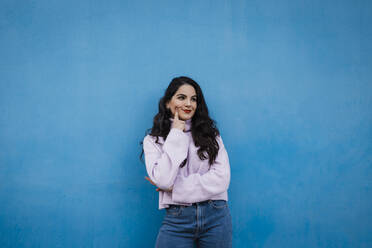 Thoughtful young woman standing in front of blue wall - DCRF01231