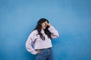Müde junge Frau vor einer blauen Wand stehend - DCRF01232