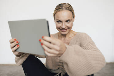 Smiling woman holding tablet PC in front of wall - RFTF00212