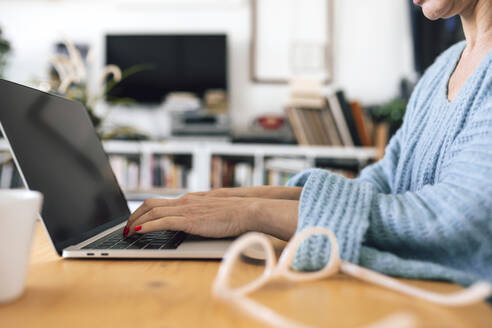 Hände einer Geschäftsfrau beim Tippen auf einem Laptop am Tisch sitzend - RFTF00235