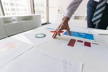 Hand eines Geschäftsmannes bei der Arbeit an Tabellen und Diagrammen am Schreibtisch im Büro - MEUF05768