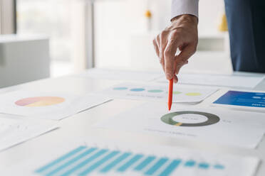 Hand of businessman with pen analyzing graphs and chart in office - MEUF05773