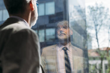 Nachdenklicher Geschäftsmann schaut durch ein Glasfenster im Büro - MEUF05780