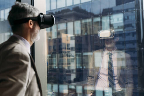 Älterer Geschäftsmann, der einen Virtual-Reality-Simulator trägt und vor einem Fenster steht - MEUF05788