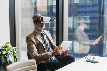 Älterer Geschäftsmann, der einen Virtual-Reality-Simulator trägt und mit einem Tablet-PC am Schreibtisch sitzt - MEUF05790