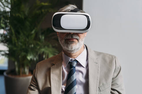 Lächelnder reifer Geschäftsmann mit Virtual-Reality-Simulator im Büro - MEUF05793