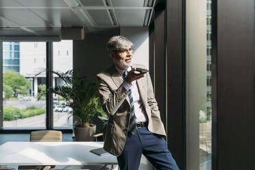 Businessman talking on smart phone standing by window in office - MEUF05822