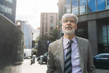 Smiling businessman wearing eyeglasses standing on sunny day - MEUF05836