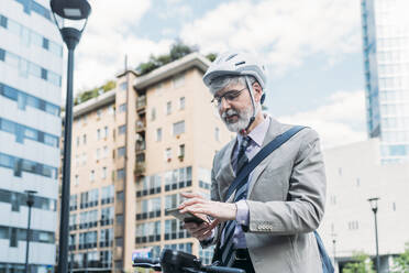 Geschäftsmann mit Fahrradhelm und Smartphone vor einem Gebäude - MEUF05838