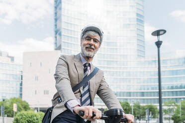 Happy businessman with electric push scooter in front of office buildings - MEUF05841